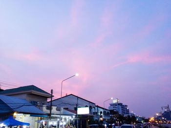 Illuminated street amidst buildings against sky at night