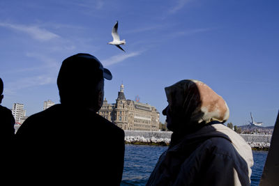 Rear view of man and seagulls flying against sky