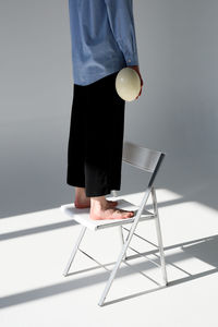 Low section of young woman standing on chair in room