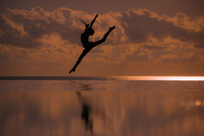 Full length of woman doing ballet dancing in infinity pool by sea against sky