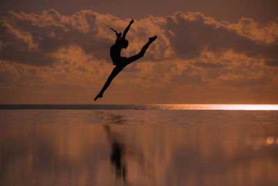 Silhouette person in sea against sky during sunset