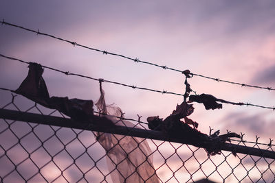 Low angle view of barbed wire fence against sky during sunset