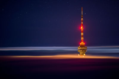 Illuminated tower amidst clouds against sky at night