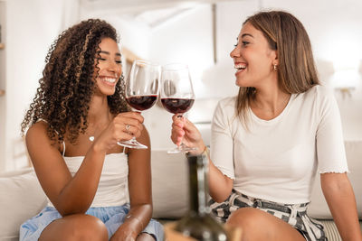 Smiling young woman drinking glass while sitting at home