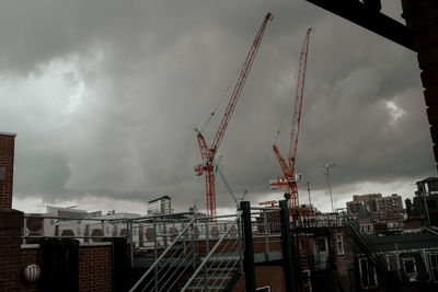 Low angle view of cranes against buildings in city