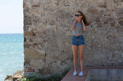 Young woman standing against wall at beach