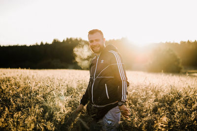 Portrait of young man standing on field against sky
