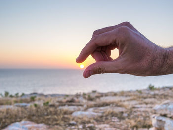 Midsection of person against sea during sunset