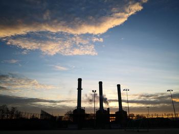 Silhouette factory against sky during sunset