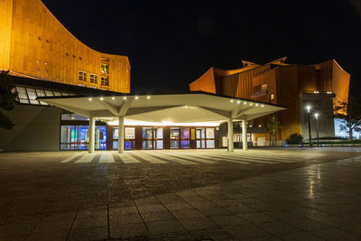 Empty road by illuminated buildings against sky at night