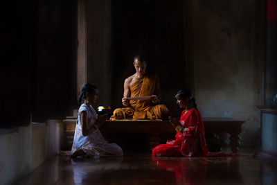 Women praying while sitting by monk in temple