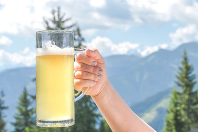 Close-up of hand holding beer glass against mountain