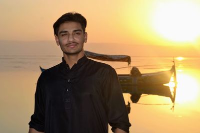 Portrait of young man standing against sea during sunset