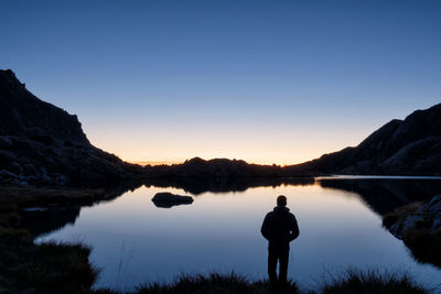 Silhouette man standing by lake against sky during sunset