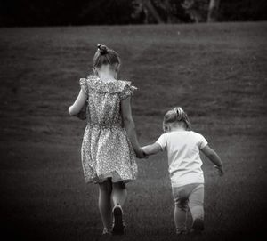 Rear view of girls holding hands while walking on field