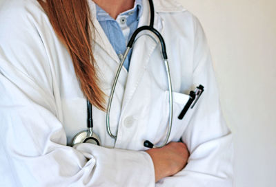 Midsection of female doctor with arms crossed over white background