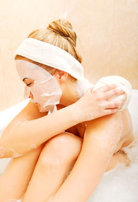 Woman rubbing shoulder with sponge in bathtub at bathroom