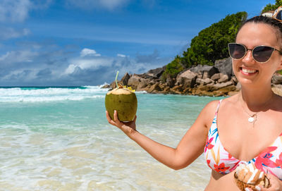 Beautiful young woman wearing bikini, holding fresh coconut with coconut water on tropical beach