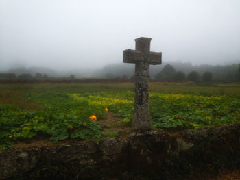 Cross on grassy field against sky during foggy weather