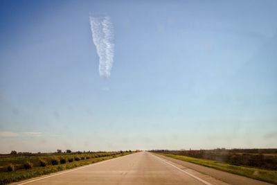 Empty road amidst field against blue sky