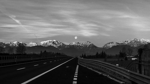 Empty road leading towards mountains against sky