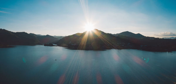 Scenic view of lake and mountains against bright sun