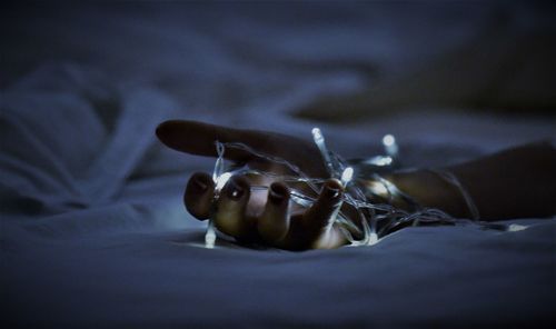 Cropped hand of woman with illuminated string lights on bed