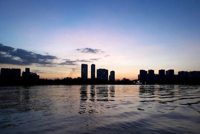 Buildings by sea against sky during sunset