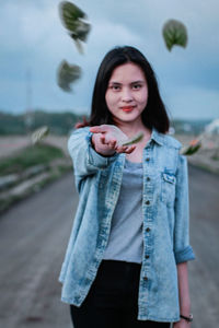 Portrait of beautiful young woman amidst leaves against sky