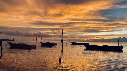 Sailboats moored on sea against sky during sunset