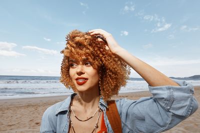 Portrait of young woman standing at beach against sky