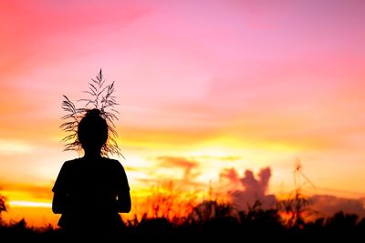 Rear view of silhouette woman standing on field against sky during sunset