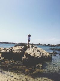 Man standing on rock at sea shore against sky