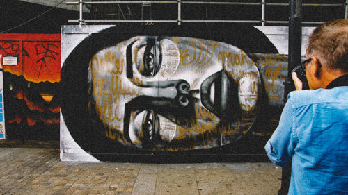 Rear view of man standing by graffiti on wall