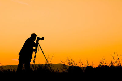 Silhouette man photographing against orange sky
