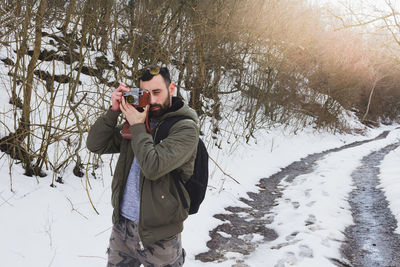 Man photographing while standing on snow covered tree