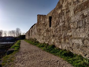 Road passing through stone wall against sky