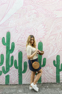 Full length portrait of woman standing against graffiti wall