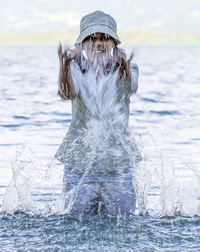 Woman with clothes and hat standing and splashing in the water in locarno, switzerland.