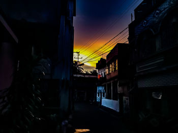 Street amidst buildings against sky at sunset