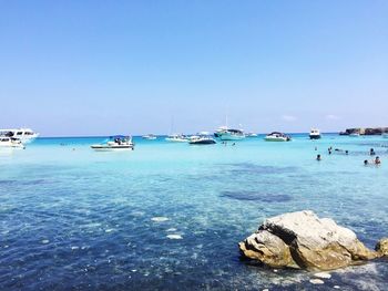 Boats moored in sea against clear blue sky