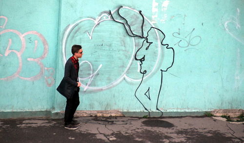 Side view of man standing against graffiti wall