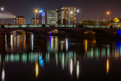 Illuminated city by river against sky at night