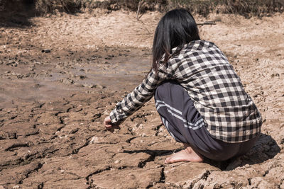 Rear view of woman crouching on barren land