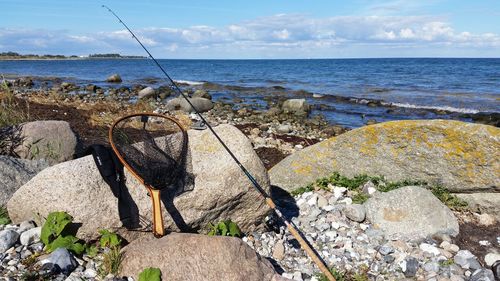 Fishing net and rod at beach against sky