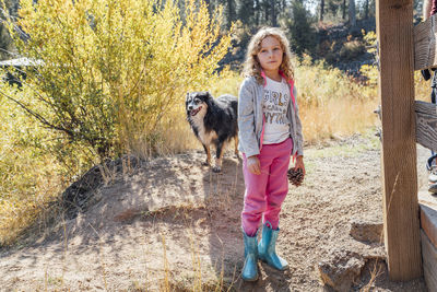 Girl holding pine cone standing in field in autumn with dog