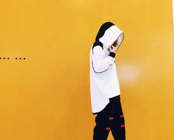 Fashionable woman wearing white hooded shirt while walking against yellow wall