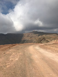 Dirt road passing through landscape against sky