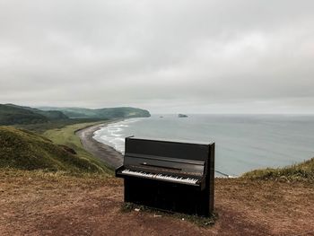 Piano on mountain by sea against cloudy sky