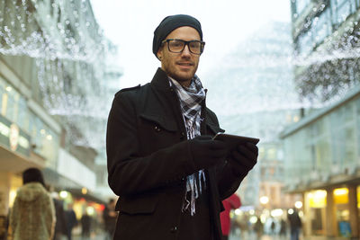 Portrait of man wearing warm clothing using digital tablet in city